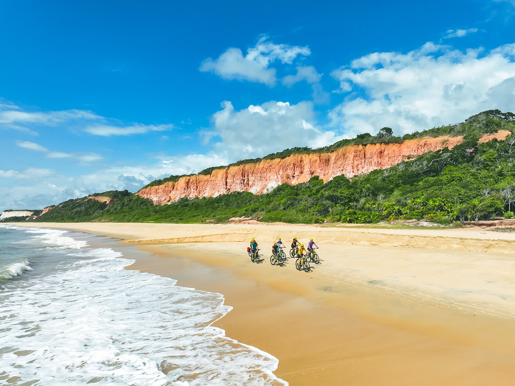 Cyclists on a red-cliff beach on the Brazilian coast